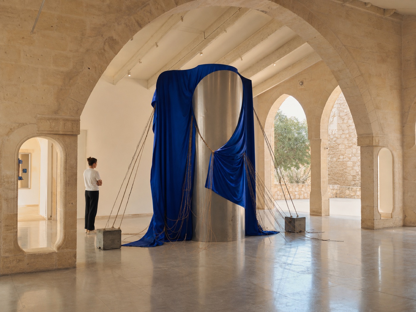 Blue textile and metal installation in a sunlit stone gallery